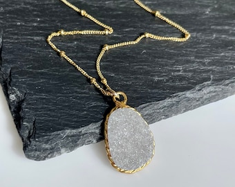 May include: A gold chain necklace with a white, sparkly, oval-shaped pendant. The pendant has a gold, rope-like border.