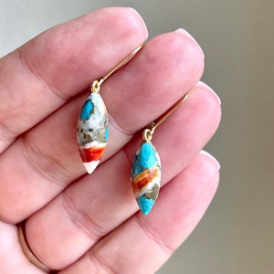 May include: A pair of gold dangle earrings with turquoise, white, and orange stone drops.