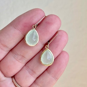 Puede incluir: Un par de pendientes de gota de oro con detalles de piedras preciosas verde claro.
