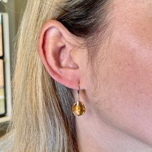 May include: A pair of gold teardrop earrings with a light amber gemstone.