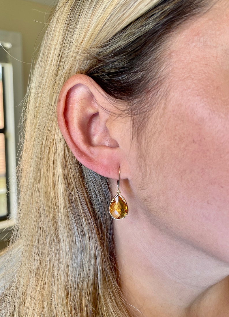 May include: A pair of gold teardrop earrings with a light amber gemstone.