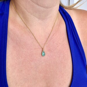 Puede incluir: Un collar de cadena de oro con un colgante de piedra preciosa azul claro en forma de l&aacute;grima.