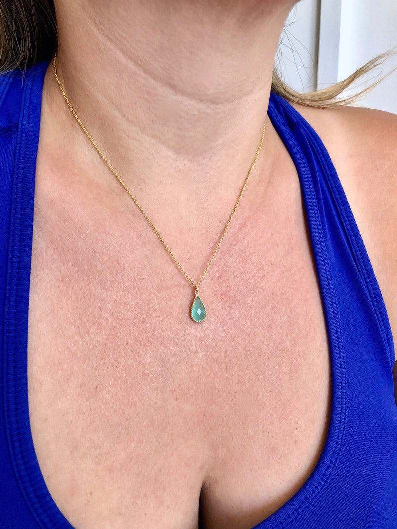 Puede incluir: Un collar de cadena de oro con un colgante de piedra preciosa azul claro en forma de l&aacute;grima.