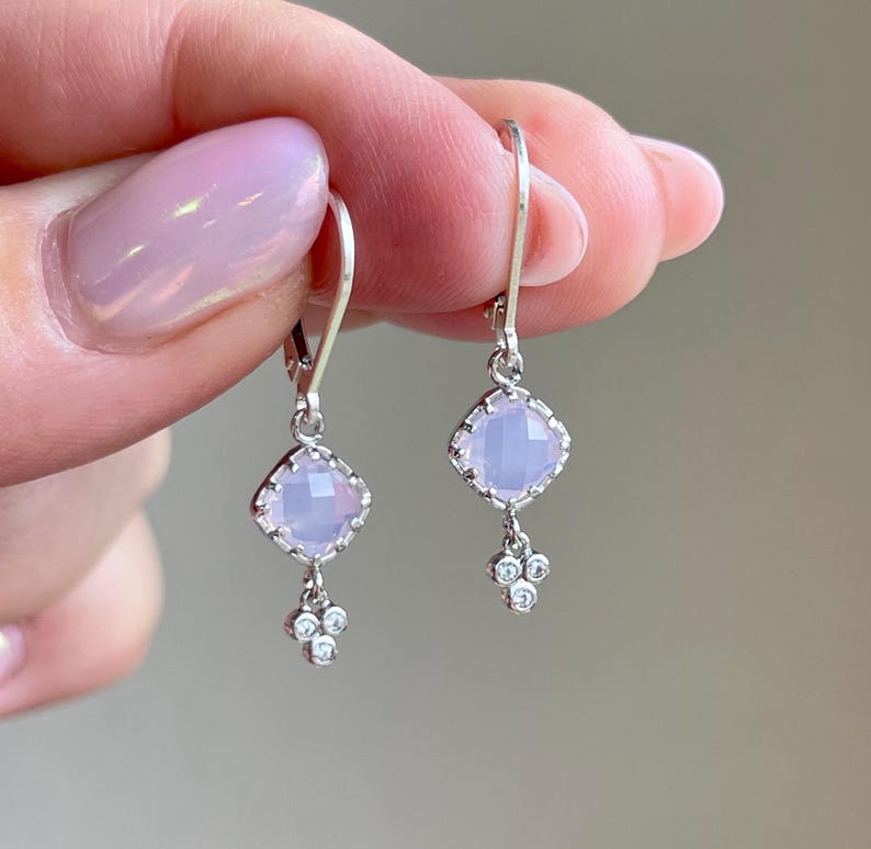May include: Silver dangle earrings with a light purple square gemstone and a cluster of smaller clear gemstones.