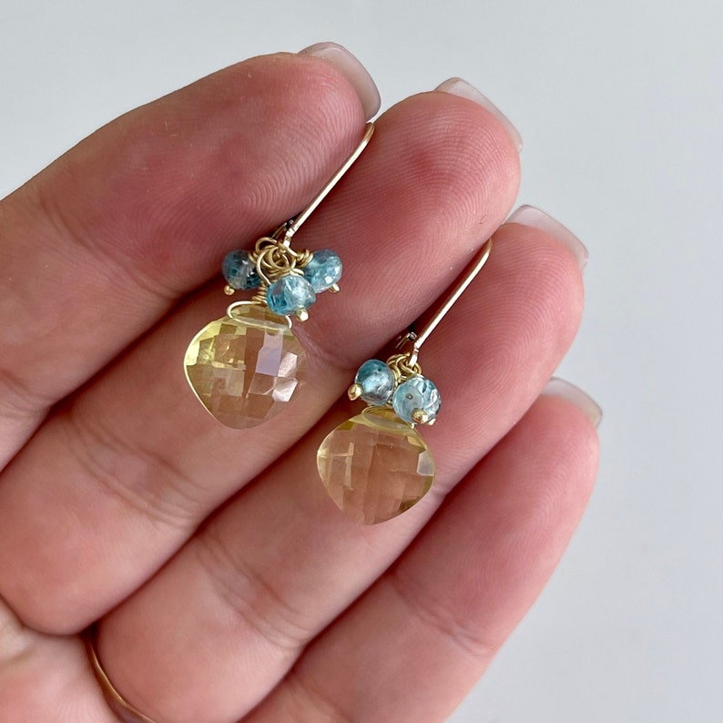 May include: Gold earrings with a teardrop-shaped yellow citrine gemstone and blue topaz accents.