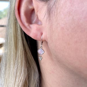 May include: Silver dangle earrings with a light pink gemstone and a small cluster of clear gemstones.