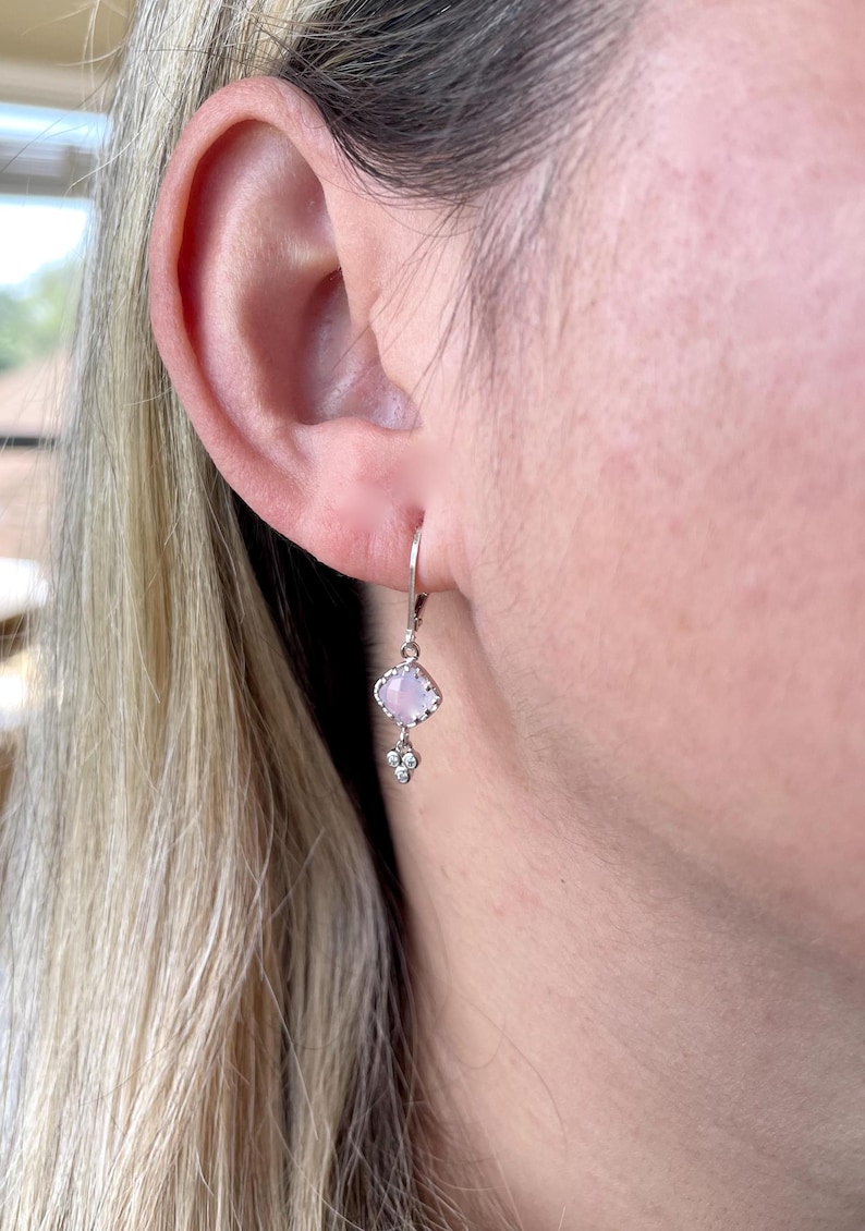 May include: Silver dangle earrings with a light pink gemstone and a small cluster of clear gemstones.