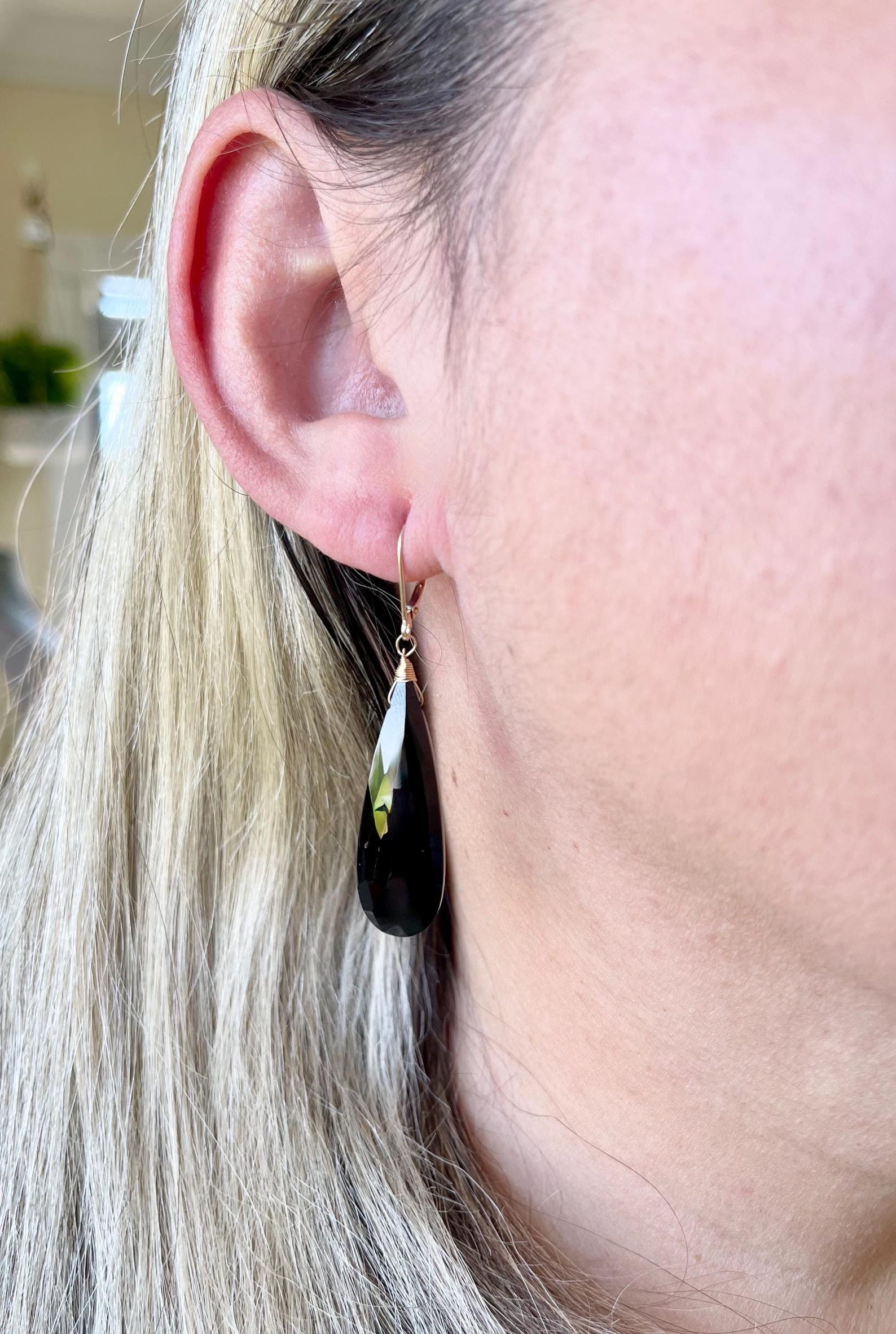 Long black onyx teardrop earring worn in ear with subtle shine and gold hook