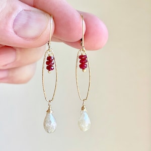 May include: Gold earrings with a teardrop-shaped white gemstone and a cluster of red gemstones.