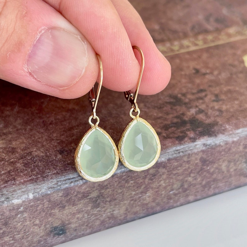 Puede incluir: Un par de pendientes de gota de oro con detalles de piedras preciosas verde claro.