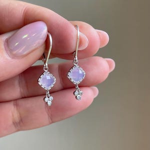 May include: A pair of silver dangle earrings with a light purple square gemstone and three small clear gemstones hanging from each.
