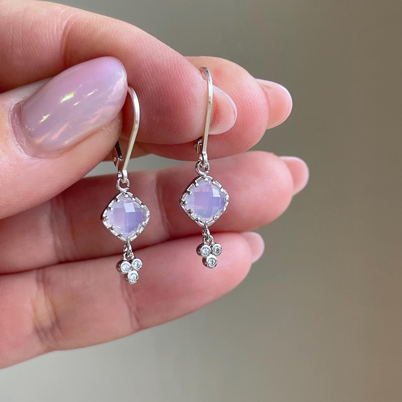 May include: A pair of silver dangle earrings with a light purple square gemstone and three small clear gemstones hanging from each.