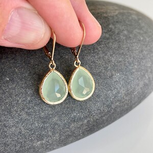 Puede incluir: Un par de pendientes en forma de l&aacute;grima con una piedra preciosa verde claro y engastes de metal dorado.