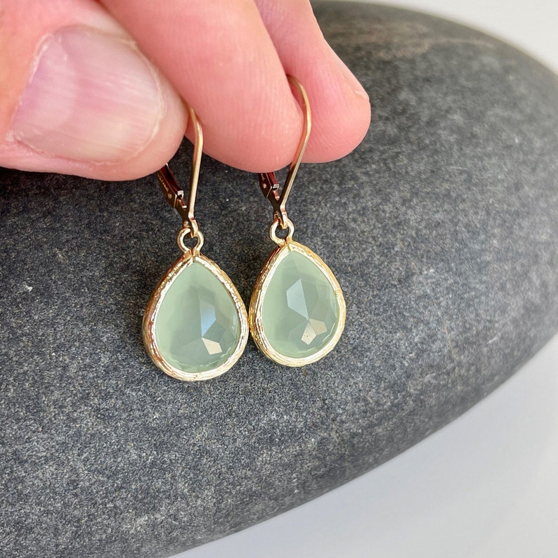 Puede incluir: Un par de pendientes en forma de l&aacute;grima con una piedra preciosa verde claro y engastes de metal dorado.