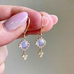 May include: A pair of gold earrings with a pink gemstone and small diamonds dangling below.