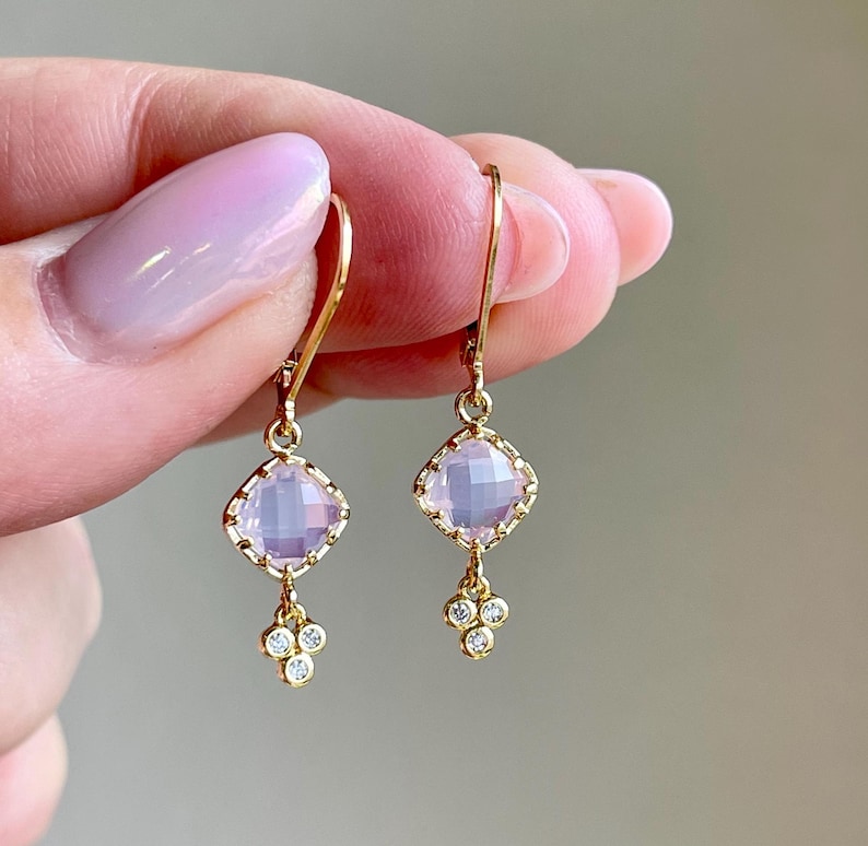 May include: A pair of gold earrings with a pink gemstone and small diamonds dangling below.