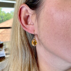 May include: Gold teardrop earrings with a yellow gemstone.