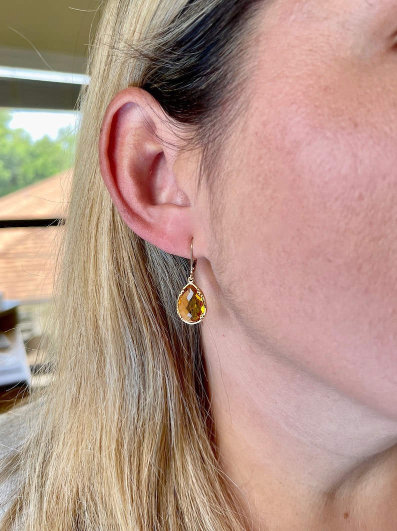 May include: Gold teardrop earrings with a yellow gemstone.