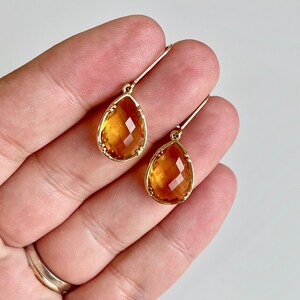 May include: A pair of gold teardrop earrings with amber-colored faceted stones.