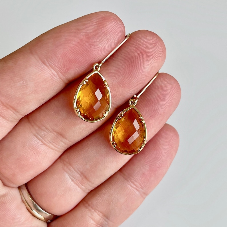 May include: A pair of gold teardrop earrings with amber-colored faceted stones.