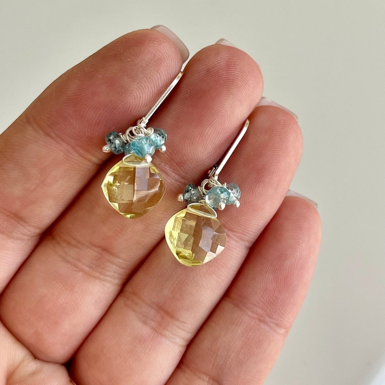 May include: A pair of silver earrings with a yellow gemstone and blue accents. The earrings are dangle style and feature a faceted yellow gemstone with a cluster of smaller blue gemstones.