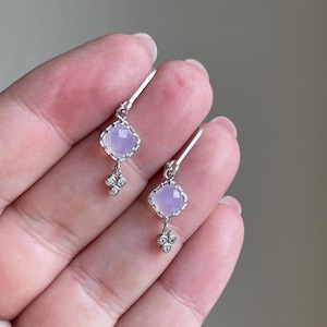 May include: A pair of silver earrings with a light purple square gemstone and three small clear gemstones dangling below.