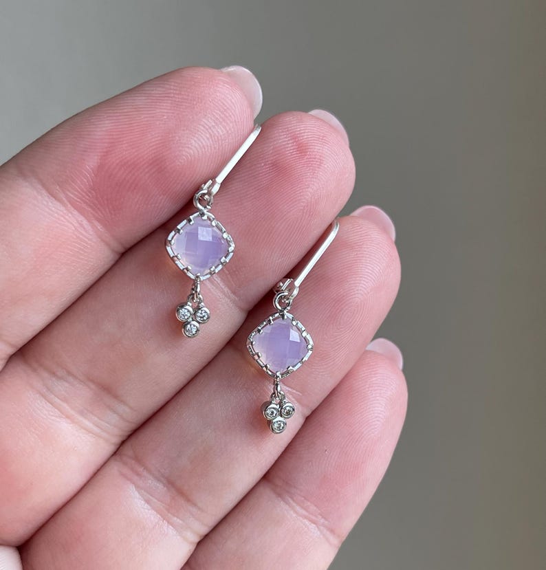 May include: A pair of silver earrings with a light purple square gemstone and three small clear gemstones dangling below.