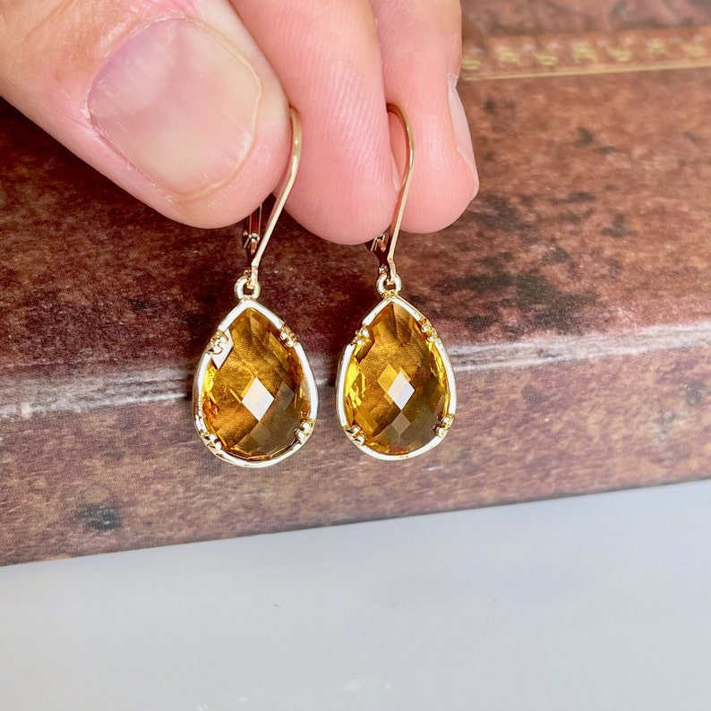 May include: A pair of gold teardrop earrings with amber-colored gemstone drops. The earrings have a delicate, intricate design.