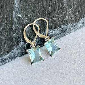 May include: A pair of silver dangle earrings with light blue square-shaped gemstones.