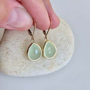 Puede incluir: Un par de pendientes de gota de oro con detalles de piedras preciosas verde claro.