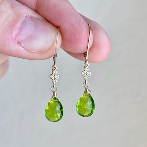 May include: Gold earrings with a teardrop-shaped green peridot gemstone and a cluster of small diamonds.