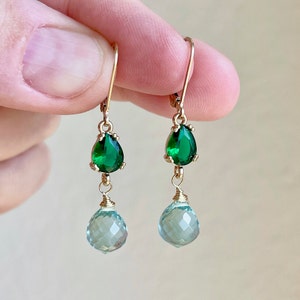 May include: Gold dangle earrings with a teardrop shaped green gemstone and a smaller round light blue gemstone.