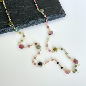 Pode incluir: Um colar longo de corrente dourada com gemas rosa, verdes e pretas. O colar &eacute; feito de pequenas contas douradas e gemas maiores de forma irregular.