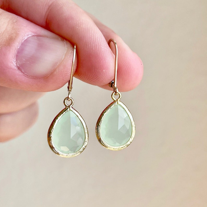 Puede incluir: Un par de pendientes de gota de oro con piedras de vidrio facetadas de color verde claro.