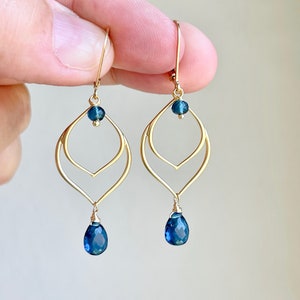 May include: Gold earrings with a double teardrop design and blue gemstone accents.