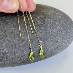 May include: A pair of gold chain earrings with green gemstone drops. The earrings are delicate and dangle from the earlobe.