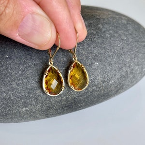 May include: A pair of gold teardrop earrings with amber-colored gemstones. The earrings have a delicate, intricate design.