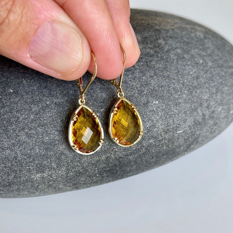 May include: A pair of gold teardrop earrings with amber-colored gemstones. The earrings have a delicate, intricate design.
