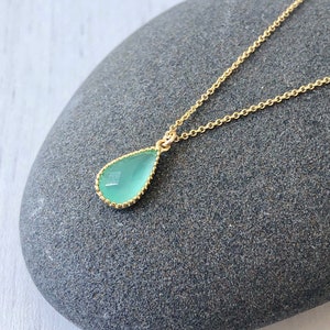 Puede incluir: Un delicado collar de cadena dorada con un colgante en forma de l&aacute;grima con una piedra preciosa azul claro.