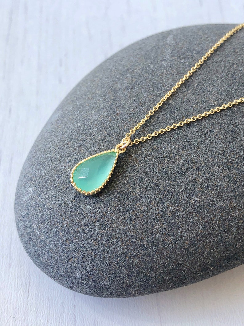 Puede incluir: Un delicado collar de cadena dorada con un colgante en forma de l&aacute;grima con una piedra preciosa azul claro.