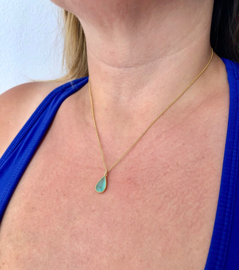 Puede incluir: Un collar de cadena de oro con un colgante en forma de l&aacute;grima con una piedra preciosa azul claro.