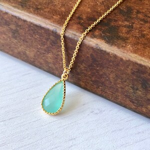 Puede incluir: Un delicado collar de cadena dorada con un colgante de piedra preciosa verde en forma de l&aacute;grima. El colgante tiene un borde dorado.