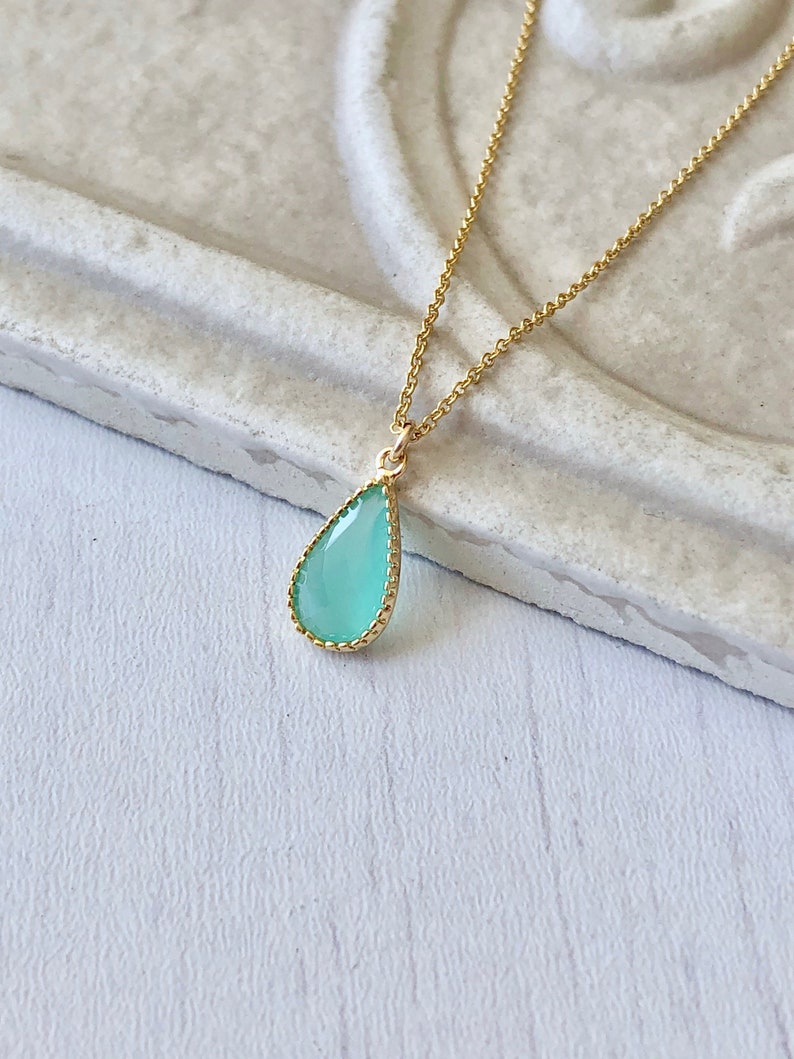 Puede incluir: Un delicado collar de cadena dorada con un colgante en forma de l&aacute;grima. El colgante est&aacute; hecho de vidrio azul claro con un borde dorado.