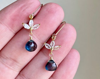 May include: Gold earrings with a teardrop shaped blue gemstone and a flower design with clear stones.