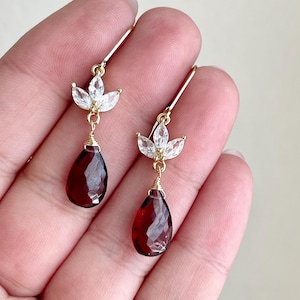 May include: A pair of gold earrings with a teardrop-shaped red gemstone and a cluster of clear stones in the shape of a flower.