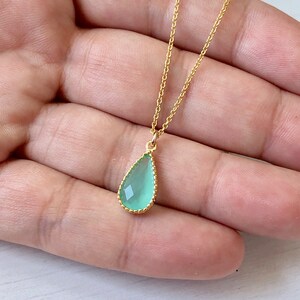 Puede incluir: Un delicado collar de cadena dorada con un colgante en forma de l&aacute;grima. El colgante est&aacute; hecho de una piedra preciosa verde claro con un borde dorado.