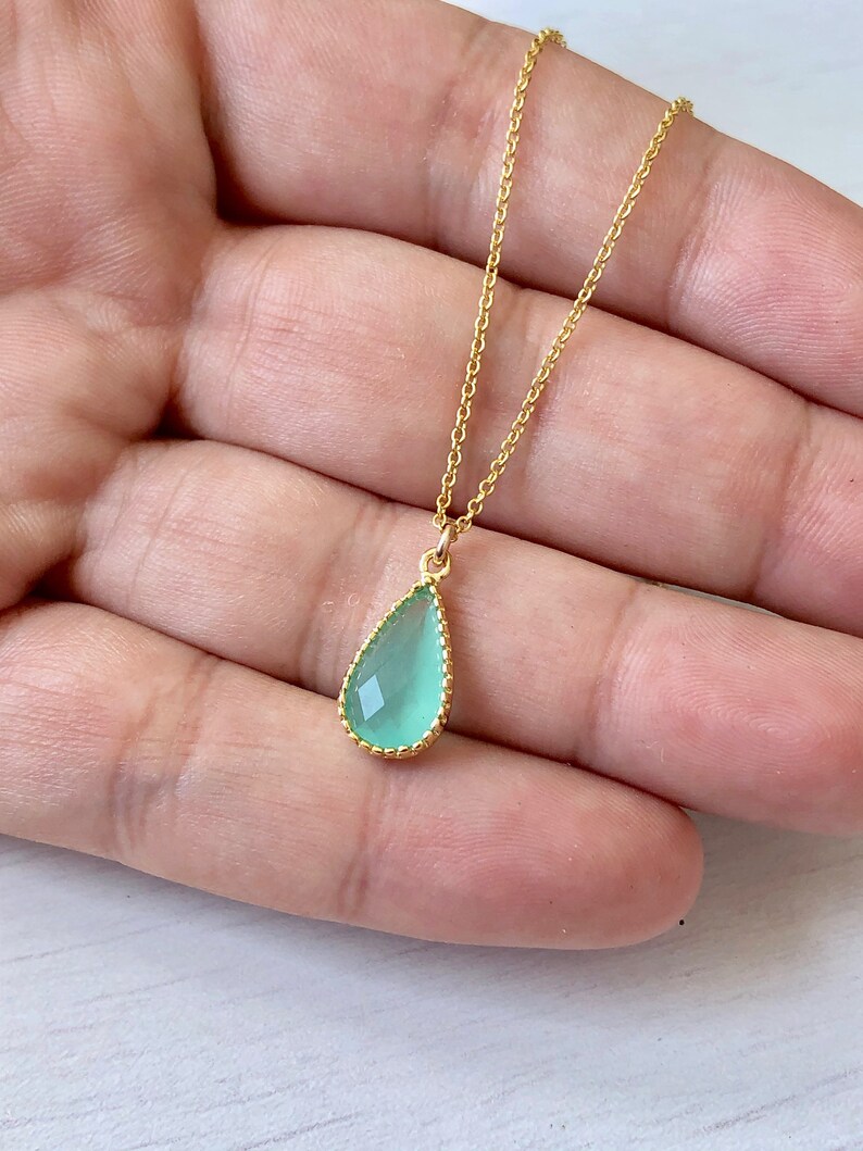 Puede incluir: Un delicado collar de cadena dorada con un colgante en forma de l&aacute;grima. El colgante est&aacute; hecho de una piedra preciosa verde claro con un borde dorado.
