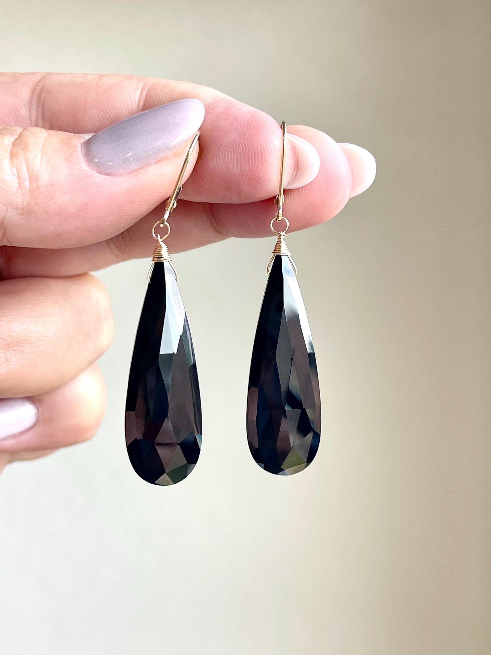Faceted black onyx teardrop earrings in 14k gold, shown held between fingers