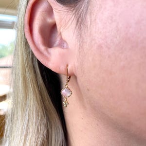 May include: Gold dangle earrings with a pink square stone and small diamond accents.