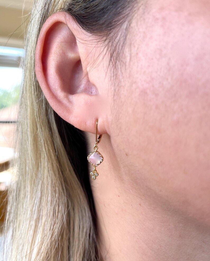 May include: Gold dangle earrings with a pink square stone and small diamond accents.